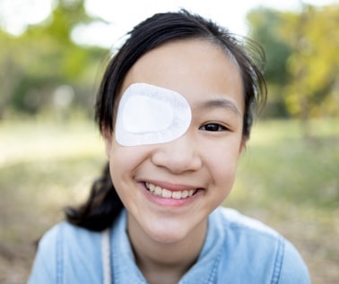 Happy young girl wears eye patching to treat child strabismus and increase muscle strength of the weaker eye.