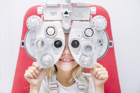 Young girl holds phoropter machine during an eye exam with a pediatric specialist in Iowa.