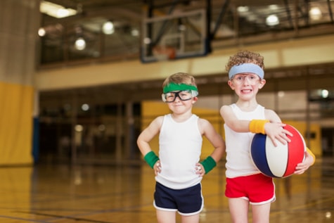 Two young boys with child protective eyewear stand and play basketball in a gymnasium in order to prevent an eye injury and eye pain.