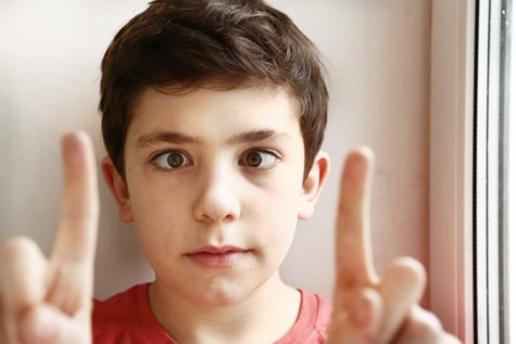 Child with childhood eye disorder, lazy eye, holds up fingers in front of his face to illustrate how his eyes are misaligned due to amblyopia. 